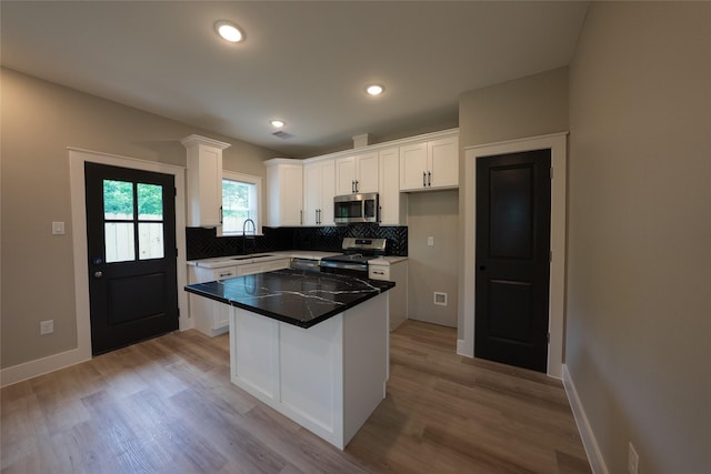 kitchen featuring appliances with stainless steel finishes, a sink, white cabinets, decorative backsplash, and light wood-style flooring