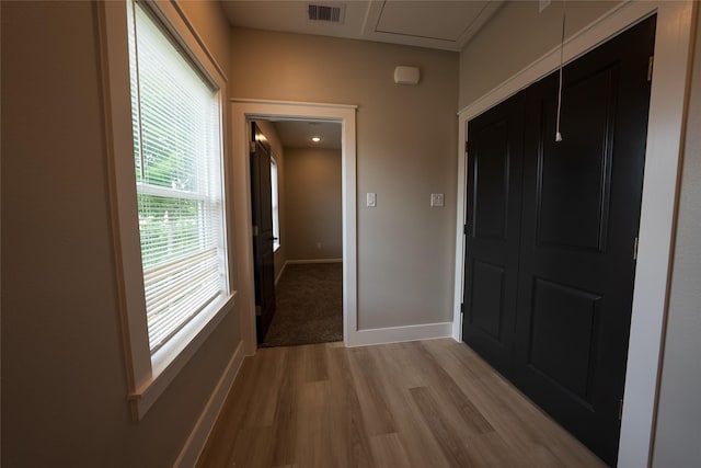 corridor with light wood-type flooring, baseboards, and attic access