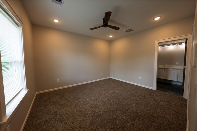 unfurnished bedroom featuring multiple windows, dark colored carpet, baseboards, recessed lighting, and ensuite bath
