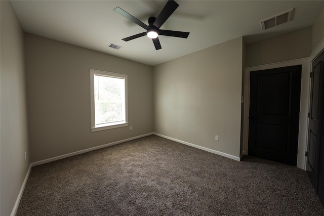 empty room featuring dark colored carpet, a ceiling fan, and baseboards