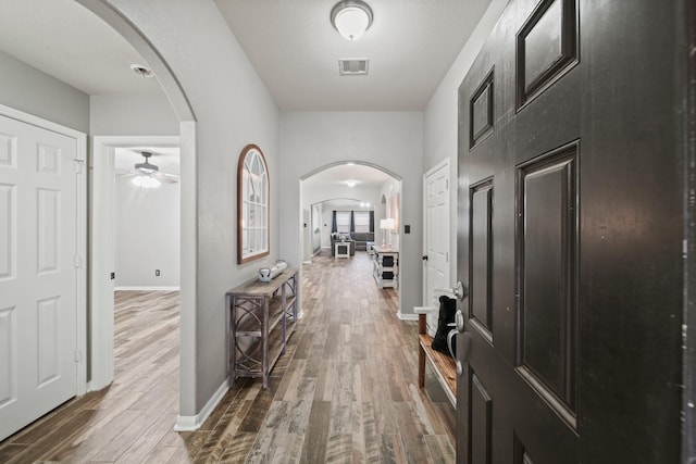 hall featuring arched walkways, wood finished floors, and baseboards