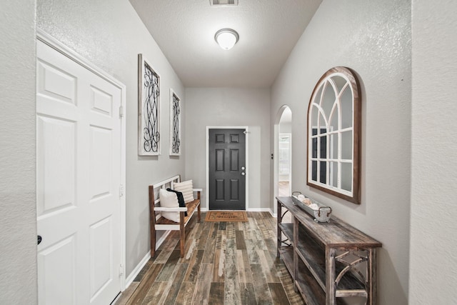 doorway to outside featuring dark wood finished floors, arched walkways, and baseboards