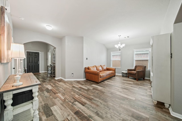 living room with arched walkways, light wood finished floors, a chandelier, and baseboards