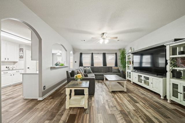 living area with a ceiling fan, wood finished floors, arched walkways, and baseboards