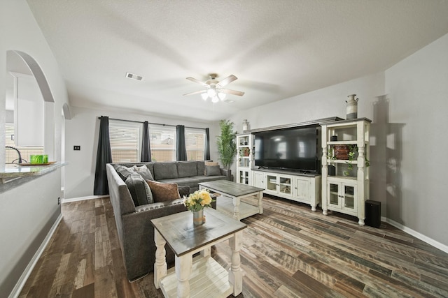 living room with a ceiling fan, baseboards, dark wood-style flooring, and arched walkways