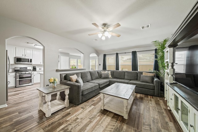 living room with wood finished floors, ceiling fan, plenty of natural light, and arched walkways