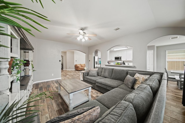 living room featuring ceiling fan, hardwood / wood-style flooring, arched walkways, baseboards, and vaulted ceiling