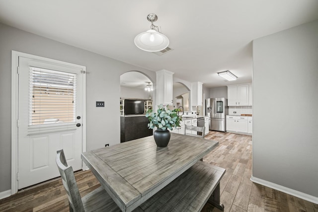 dining room with arched walkways, light wood-type flooring, and baseboards
