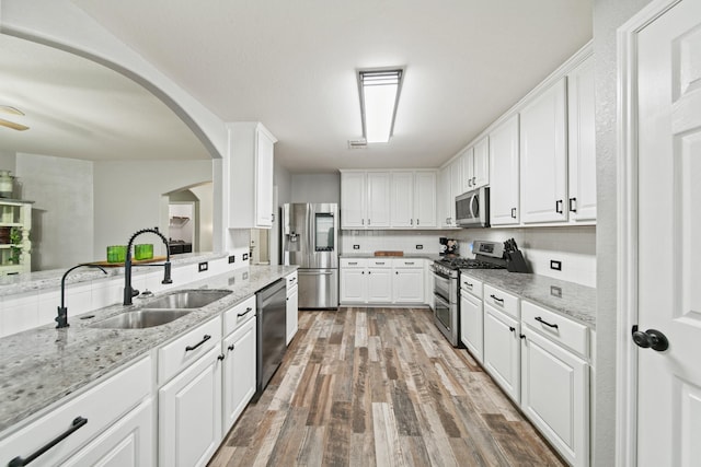 kitchen featuring appliances with stainless steel finishes, a sink, white cabinets, and wood finished floors
