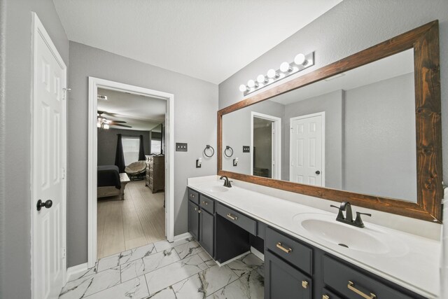 ensuite bathroom with double vanity, marble finish flooring, ceiling fan, and baseboards