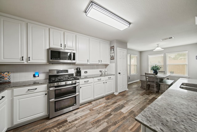 kitchen with appliances with stainless steel finishes, dark wood-style floors, decorative backsplash, and white cabinetry