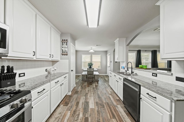 kitchen featuring a sink, appliances with stainless steel finishes, wood finished floors, arched walkways, and white cabinetry