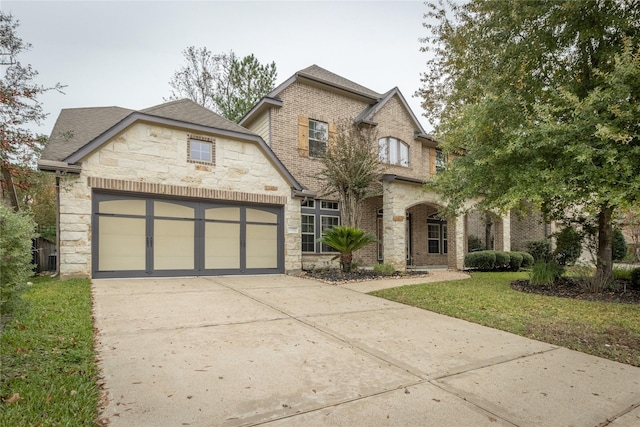 french country style house with stone siding, driveway, an attached garage, a front lawn, and a shingled roof