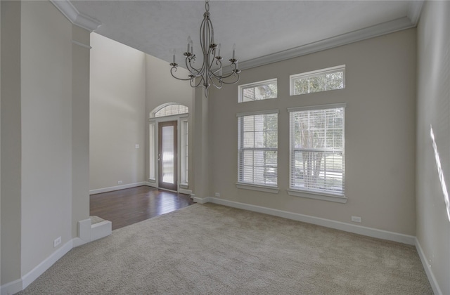 carpeted spare room featuring a chandelier, baseboards, ornamental molding, and a towering ceiling