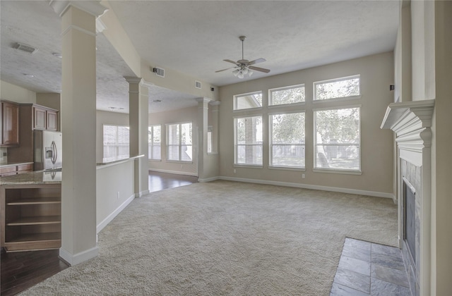 unfurnished living room featuring decorative columns, a ceiling fan, a fireplace with flush hearth, baseboards, and carpet flooring