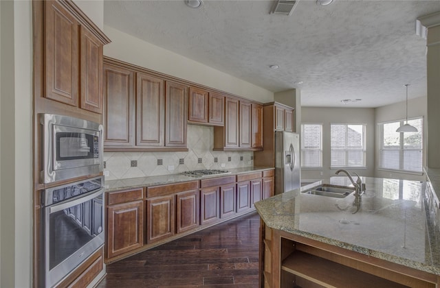 kitchen with appliances with stainless steel finishes, a sink, a textured ceiling, dark wood-type flooring, and light stone countertops