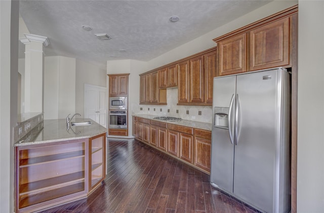 kitchen with stainless steel appliances, a sink, light stone counters, brown cabinets, and dark wood-type flooring