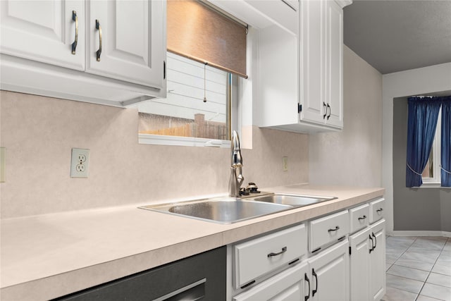 kitchen with a sink, white cabinets, light countertops, and baseboards