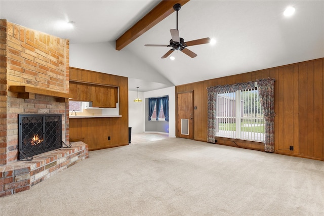 unfurnished living room with beamed ceiling, ceiling fan, light colored carpet, a fireplace, and wooden walls