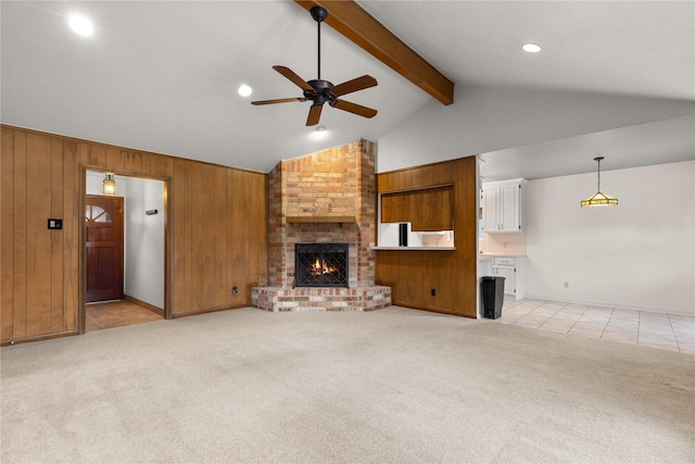 unfurnished living room with ceiling fan, light colored carpet, wooden walls, a fireplace, and beamed ceiling
