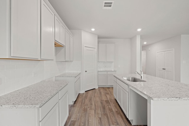 11664 Wilgers Way, Willis, TX 77378 - kitchen with a sink, wood finished floors, backsplash, a kitchen island with sink, and light stone countertops