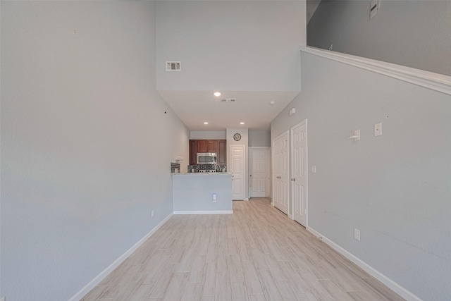unfurnished living room with light wood-style flooring, baseboards, a high ceiling, and recessed lighting