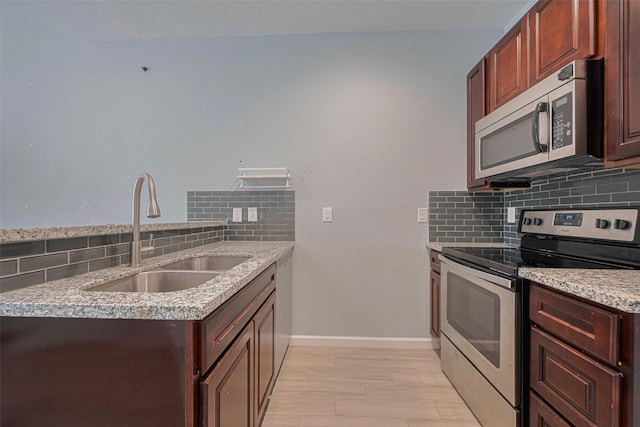 kitchen featuring stainless steel appliances, a sink, decorative backsplash, and light wood-type flooring