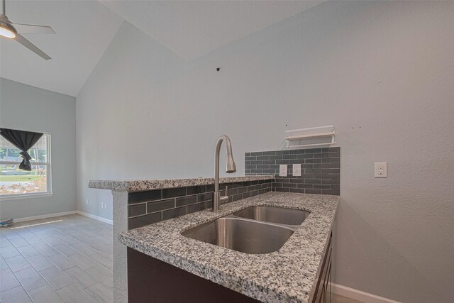kitchen featuring a sink, vaulted ceiling, decorative backsplash, light stone countertops, and baseboards