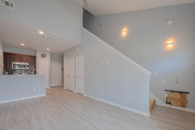 unfurnished living room with stairway, baseboards, light wood-style floors, recessed lighting, and high vaulted ceiling