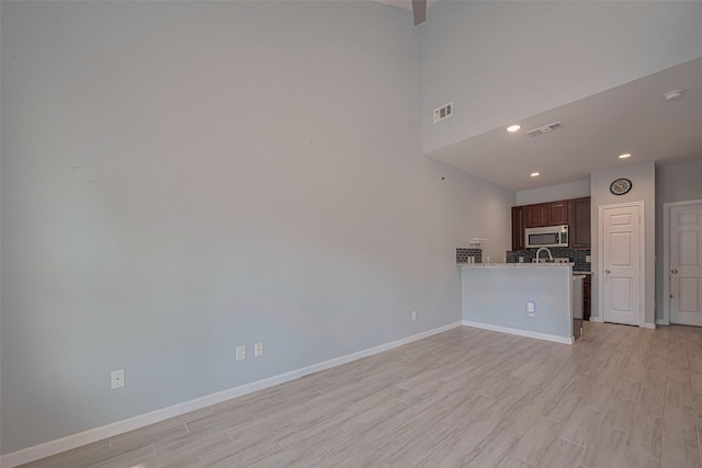 unfurnished living room featuring baseboards, light wood-style floors, recessed lighting, and a towering ceiling