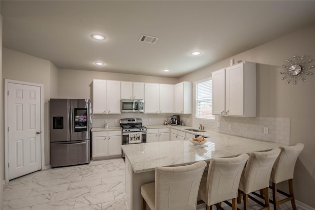 14707 Fairy Tern Ln, Houston, TX 77049 - kitchen featuring appliances with stainless steel finishes, a peninsula, light marble finish floors, white cabinets, and recessed lighting