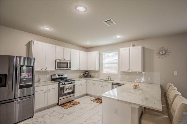 14707 Fairy Tern Ln, Houston, TX 77049 - kitchen featuring stainless steel appliances, a peninsula, a breakfast bar area, white cabinetry, and recessed lighting