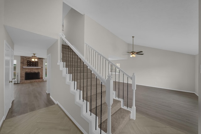 staircase with ceiling fan, a fireplace, parquet floors, baseboards, and high vaulted ceiling