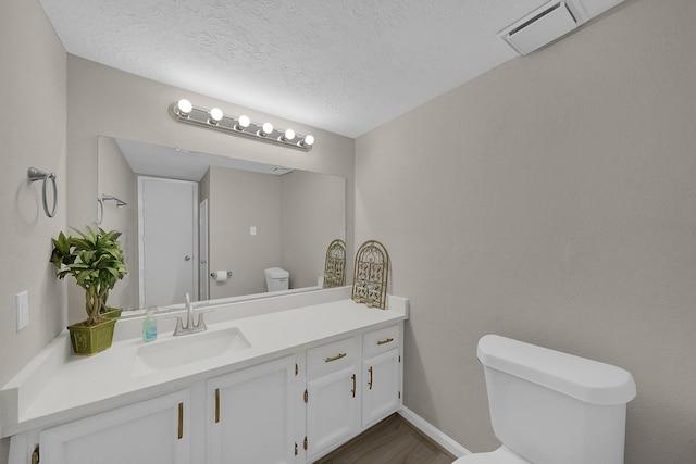 bathroom with toilet, a textured ceiling, vanity, wood finished floors, and baseboards
