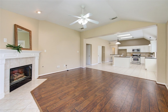 1826 Oak Lodge Dr, Pearland, TX 77581 - unfurnished living room featuring lofted ceiling, ceiling fan, light wood-type flooring, a tile fireplace, and a sink