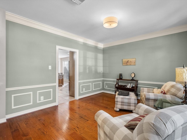 living area with crown molding, wood finished floors, and a wainscoted wall