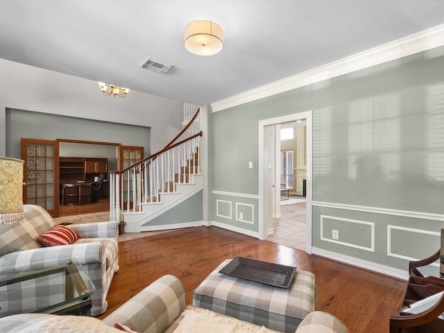 living area with stairs, a chandelier, wood finished floors, crown molding, and a wainscoted wall