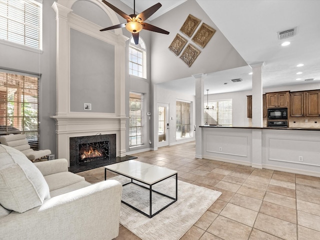 living area with a high ceiling, a premium fireplace, ornate columns, ceiling fan, and plenty of natural light