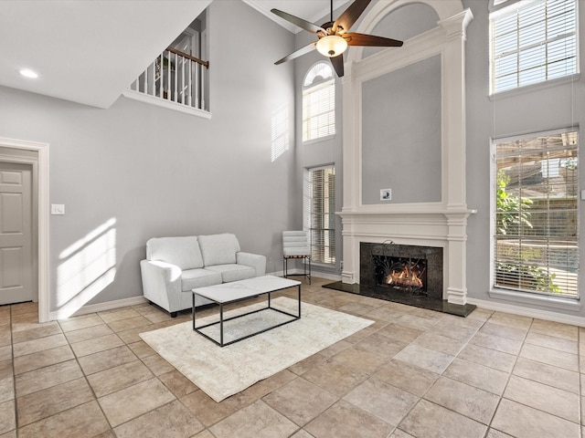 living room with a towering ceiling, ceiling fan, healthy amount of natural light, and a high end fireplace