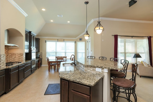 kitchen with a sink, a breakfast bar, stainless steel appliances, wall chimney range hood, and a kitchen island with sink