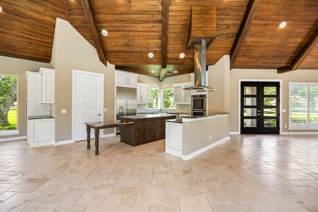 2911 S Saddlebrook Ln, Katy, TX 77494 - kitchen featuring a wooden ceiling with exposed beams, appliances with stainless steel finishes, wall chimney range hood, stone tile flooring, and plenty of natural light