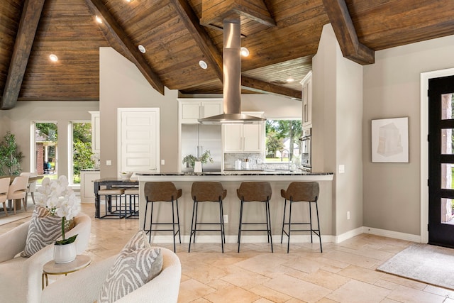 2911 S Saddlebrook Ln, Katy, TX 77494 - kitchen with a wood ceiling with exposed beams, a peninsula, white cabinetry, a kitchen bar, and stone tile floors