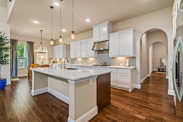 9811 Mount Shasta, Missouri City, TX 77459 - kitchen featuring under cabinet range hood, arched walkways, dark wood-style floors, a center island with sink, and decorative backsplash