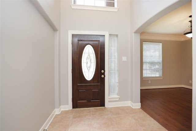 entryway featuring arched walkways, ornamental molding, baseboards, and wood finished floors