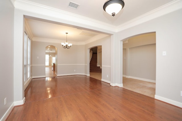 unfurnished room featuring arched walkways, a chandelier, ornamental molding, wood finished floors, and baseboards