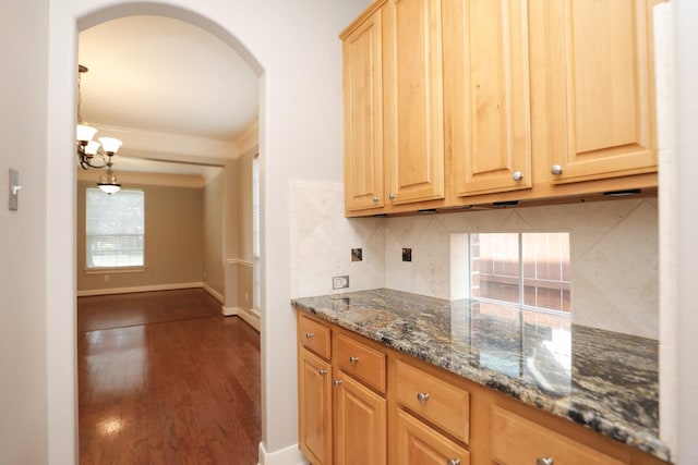 kitchen with arched walkways, backsplash, wood finished floors, dark stone counters, and crown molding