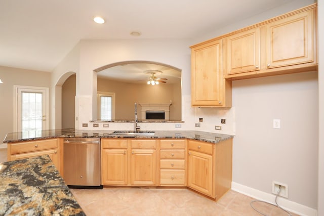 kitchen featuring dishwasher, a sink, light brown cabinets, a ceiling fan, and dark stone counters