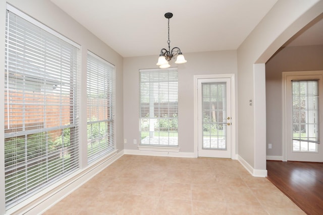 unfurnished dining area featuring a chandelier, arched walkways, baseboards, and light tile patterned floors