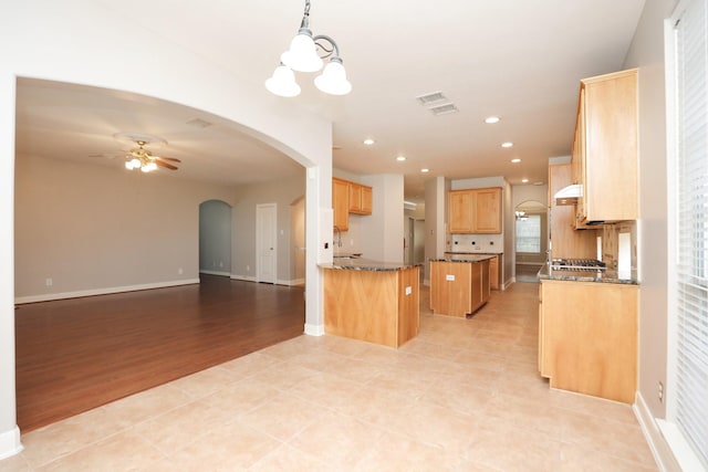 kitchen with arched walkways, open floor plan, a ceiling fan, dark stone countertops, and a chandelier