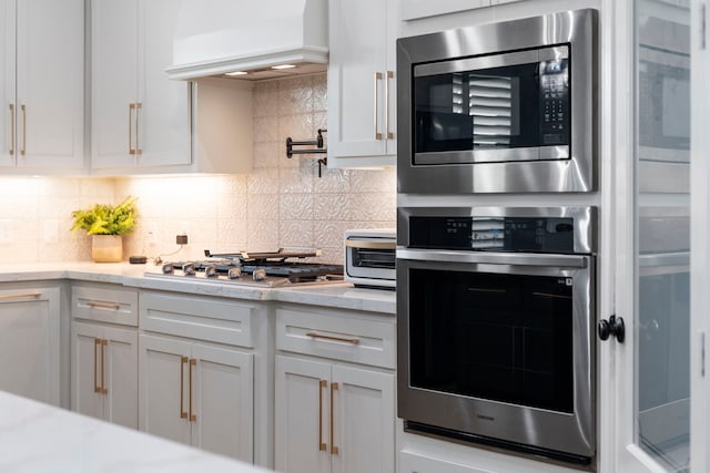 9603 Neon Moon Dr, Needville, TX 77461 - kitchen with stainless steel appliances, custom range hood, decorative backsplash, and white cabinets
